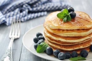 Pancakes with fresh berries, mint and maple syrup on white plate closeup